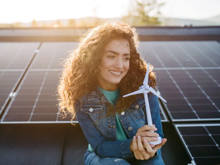 Eine Person hält ein Windturbinenmodell vor Solarpaneelen und symbolisiert nachhaltige Energieerzeugung.