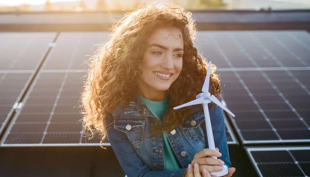 Eine Person hält ein Windturbinenmodell vor Solarpaneelen und symbolisiert nachhaltige Energieerzeugung.