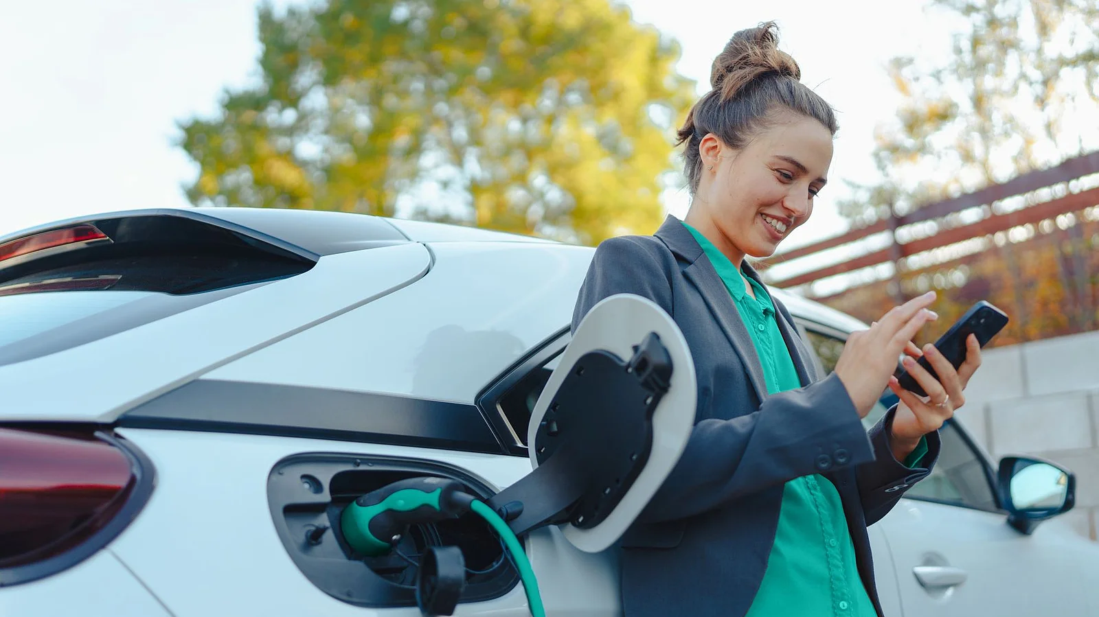 Eine Person steht neben einem Elektroauto und nutzt ein Smartphone während das Fahrzeug lädt.