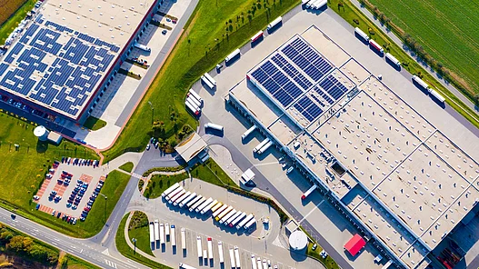 Effiziente Ladeinfrastruktur für Logistikstandorte Luftaufnahme eines großen Logistikareals mit zahlreichen LKW und Gebäuden mit Solaranlagen.