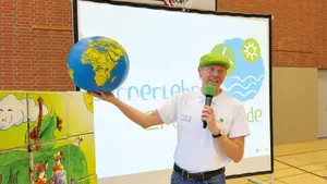 Eine Person erklärt mit Mikrofon und Globus vor Schülern das Thema Energie und Umweltbildung.