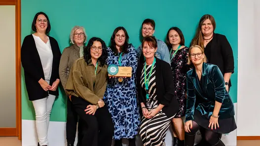 Eine Gruppe aus neun Frauen steht vor einer großen Werbewand von Westfalen Weser