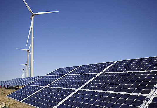 Photovoltaikanlage mit Windrädern im Hintergrund bei blauem Himmel