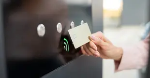 Eine Person hält eine Karte vor ein kontaktloses Zahlungsterminal mit grünem Signal-Icon.